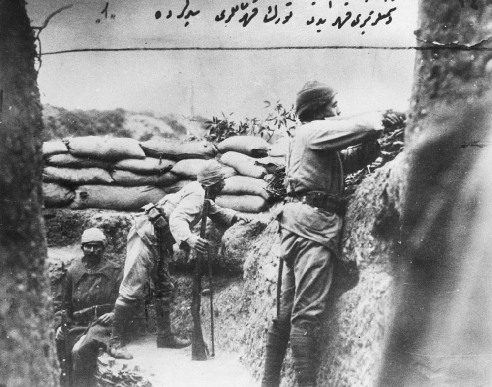 Three Turkish soldiers in a trench overlooking Australian positions. One of the men is sitting (left) while the other two men appear to be on the lookout.